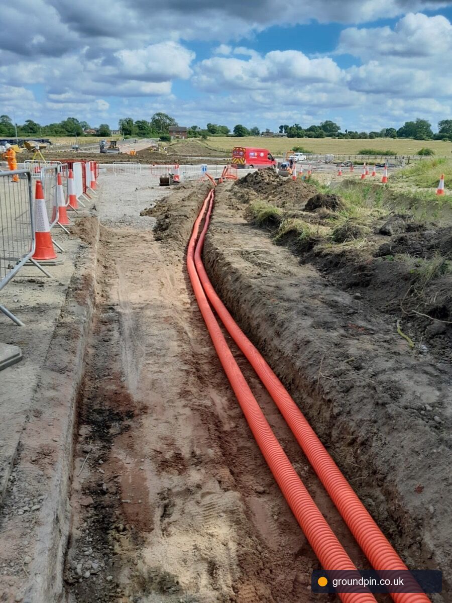 Orange utility ducts laid in a trench through open countryside