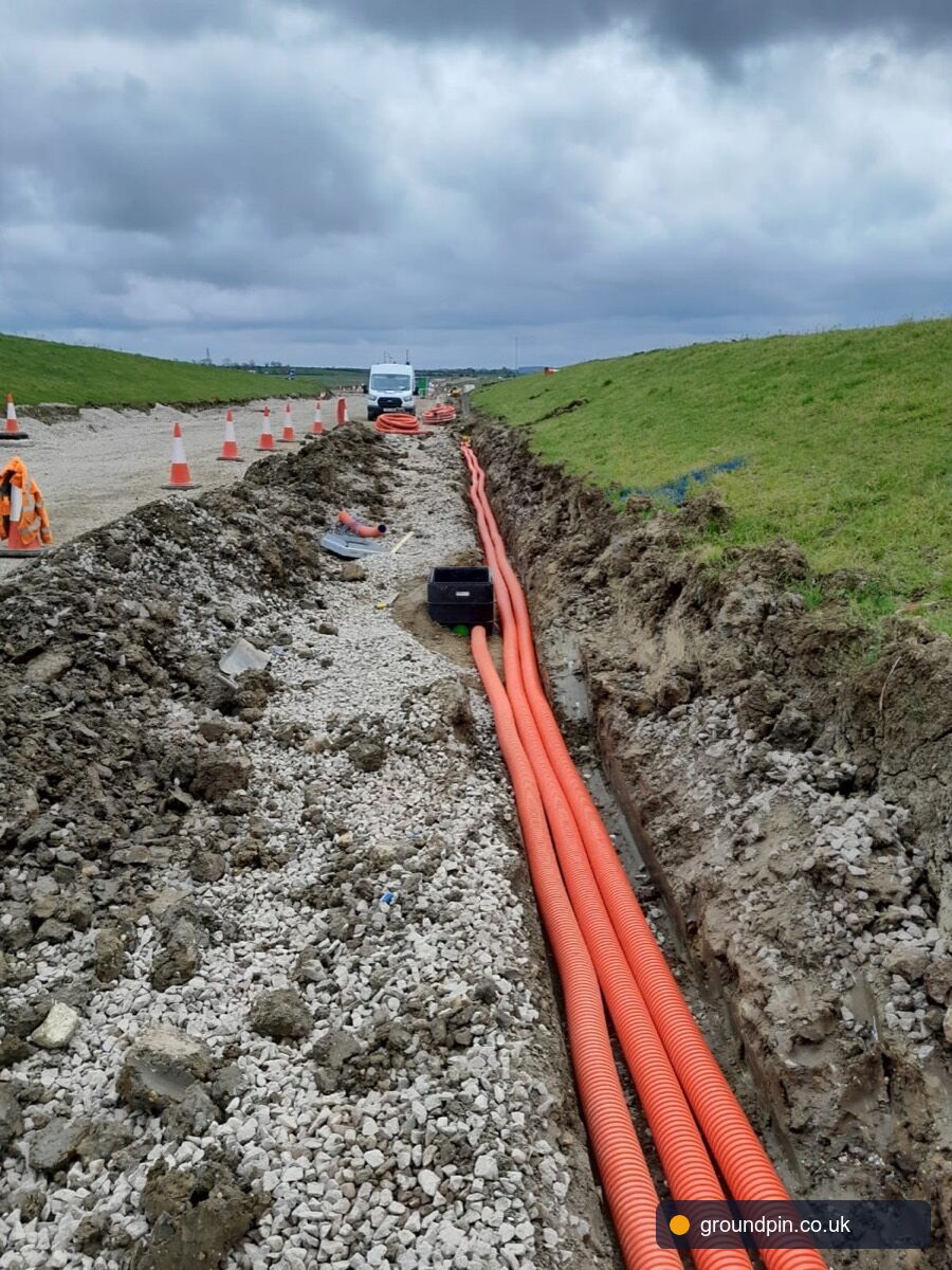Long roadside trench with orange telecoms ducts running into the distance