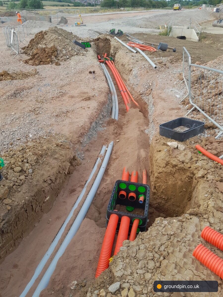 Red electric ducts, grey ducts and a green telecoms junction box in the same trench