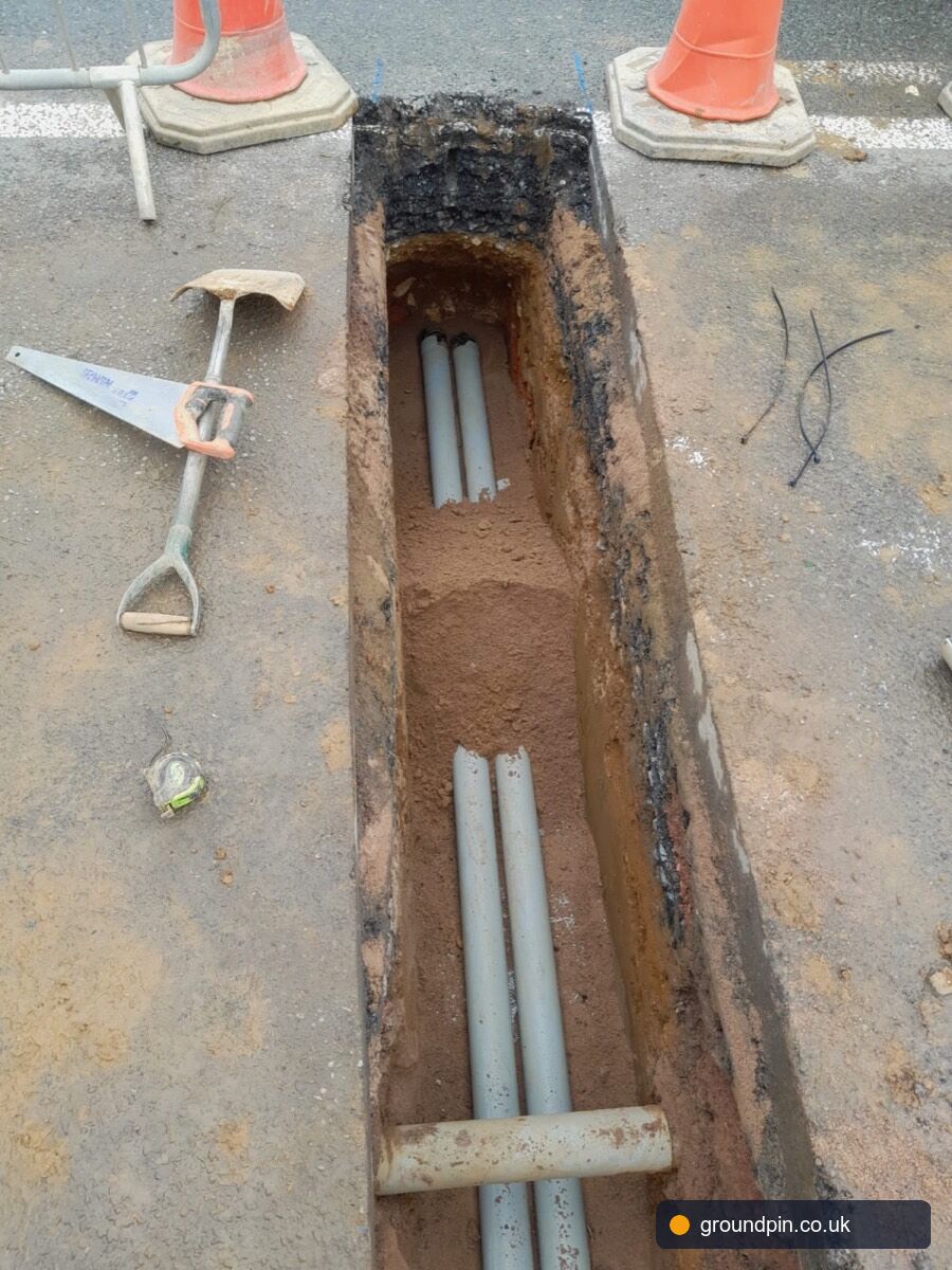 Narrow trench cut into tarmac with service ducts and tools on the road